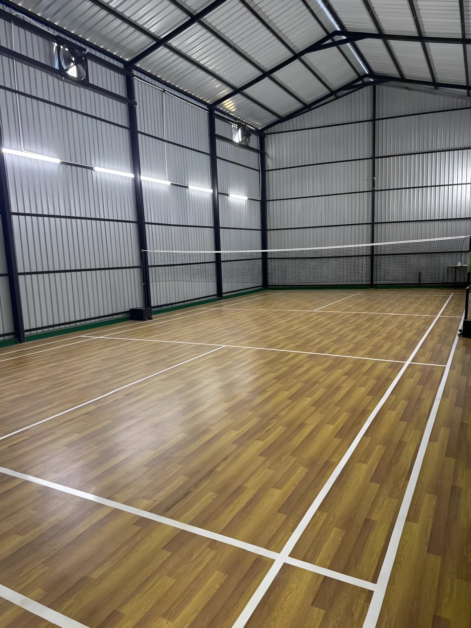 Empty wood-finish badminton court at Shuttle Point, Dehiwala, net up in a white steel-clad hall lit by strip lighting along the walls