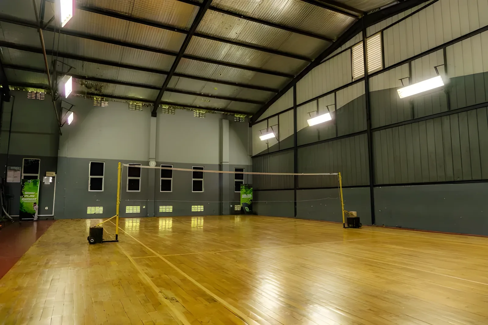 Empty wooden badminton court at Shuttle Power, Colombo 5, with the net up under a pitched steel roof and grey walls
